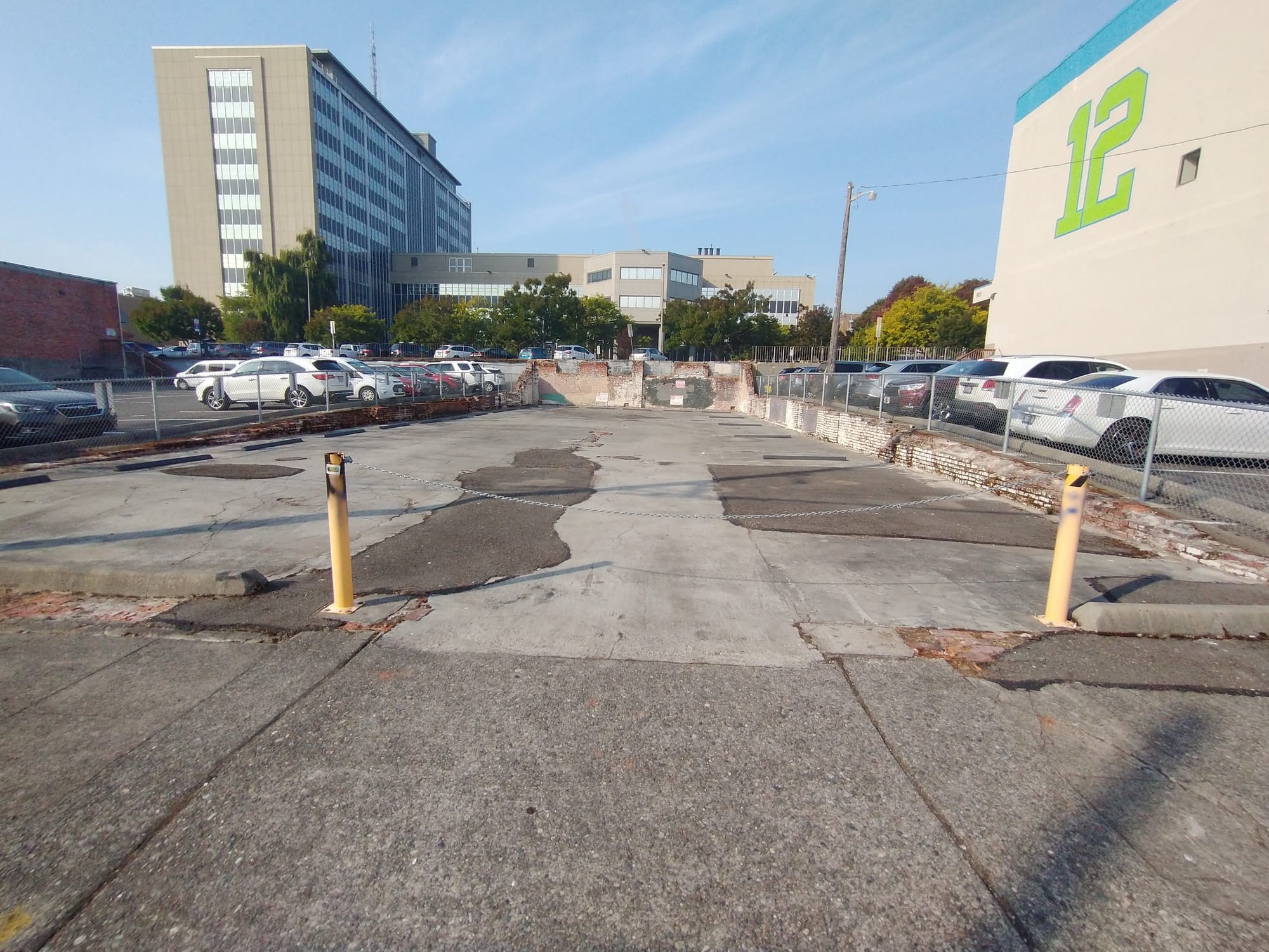 A photo of an empty lots surrounding by surface level parking and large buildings.
