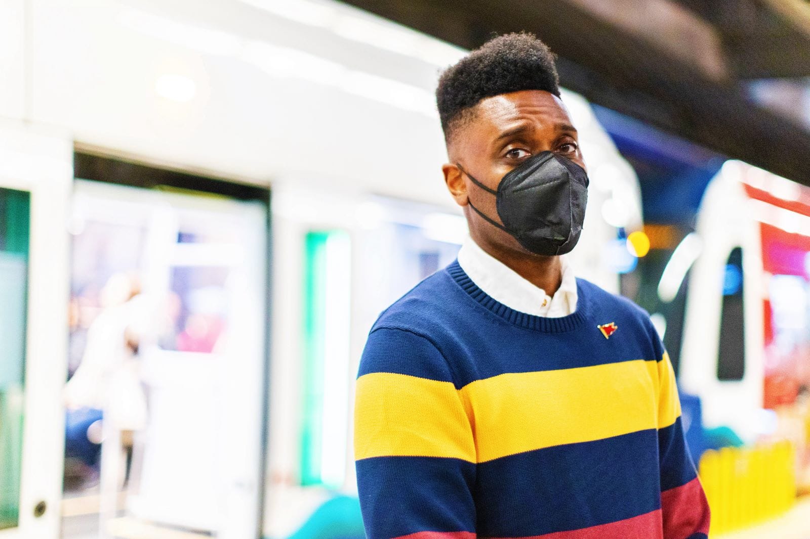 Shaun Scott is a Black man with a hi-top fade and wears an N95 mask while standing in front of a Link light rail train on a station platform.
