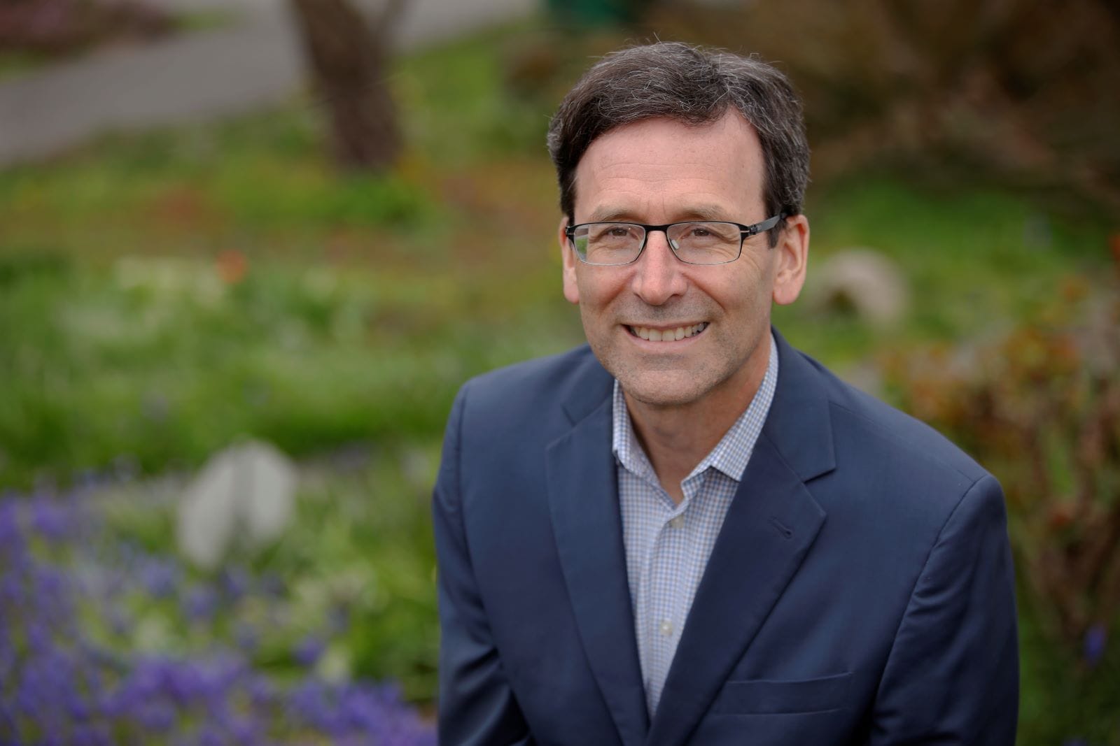 Ferguson is a middle aged White man in glasses in a suit posing by some flowers