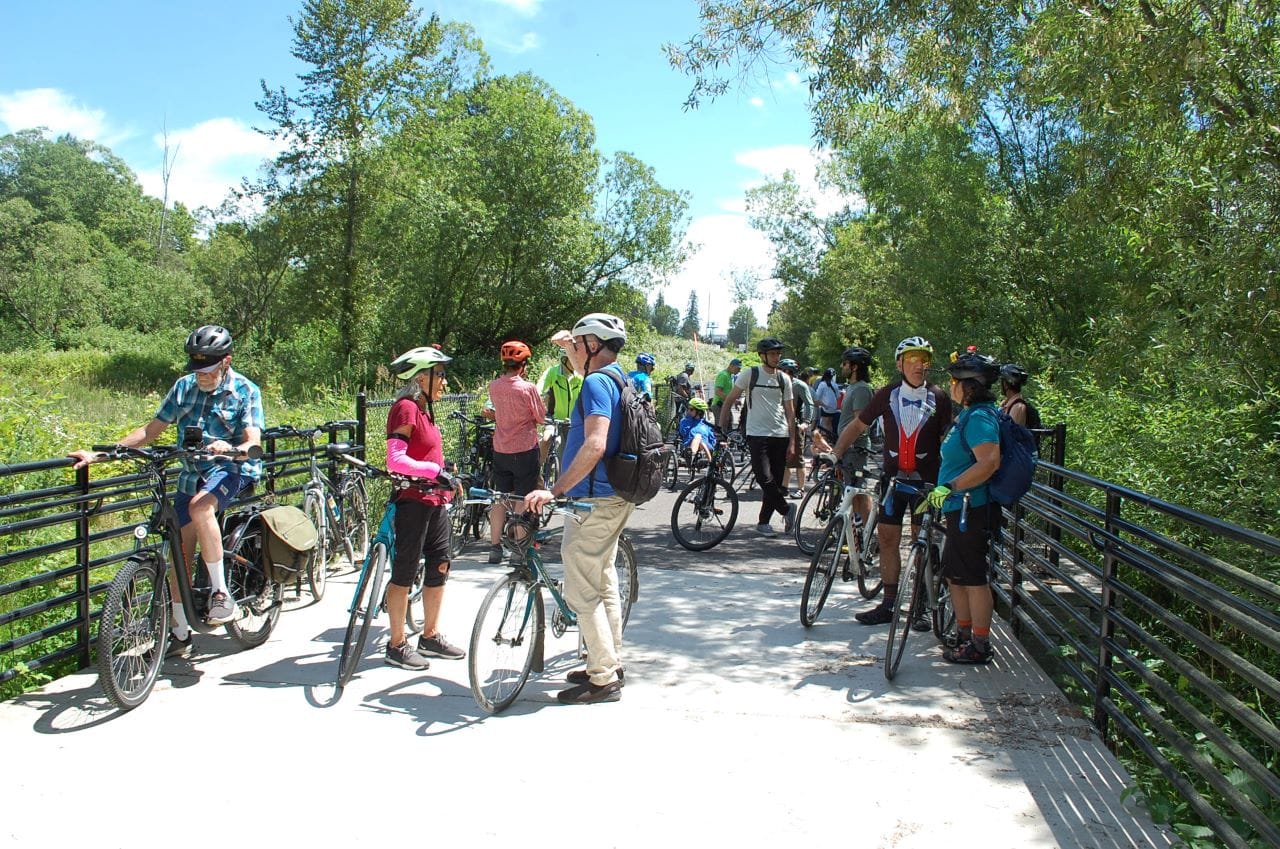 A group of over dozen people with their bikes on a wetland boardwalk segment of the trail.