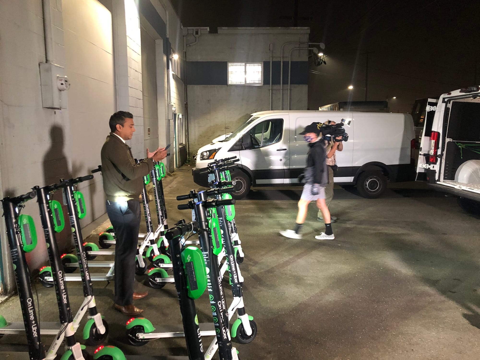
                     A reporter stands amidst scooters in a garage for a TV spot.
                     