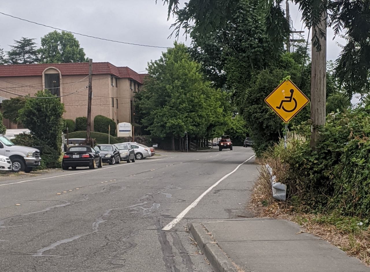 
                     A yellow sign with a wheelchair on it indicates the people rolling are to use the gutter after the sidewalk ends. They did pa
                     