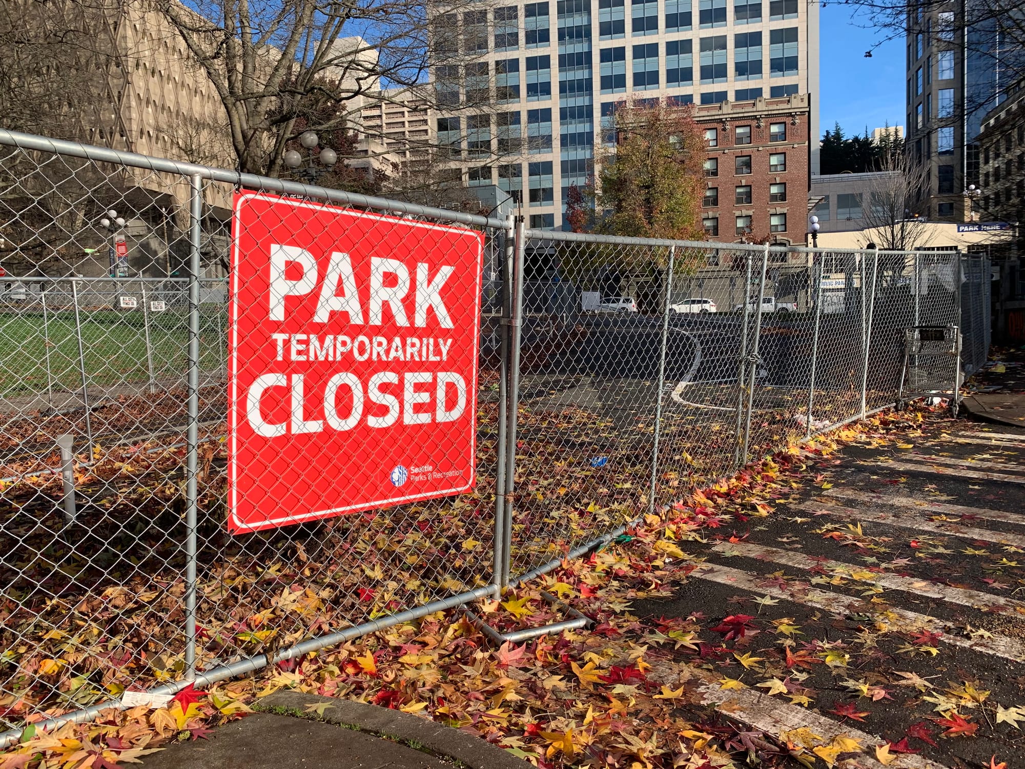 A photo of a chainlink fence and a sign reading "park closed" in front a open grassy area.