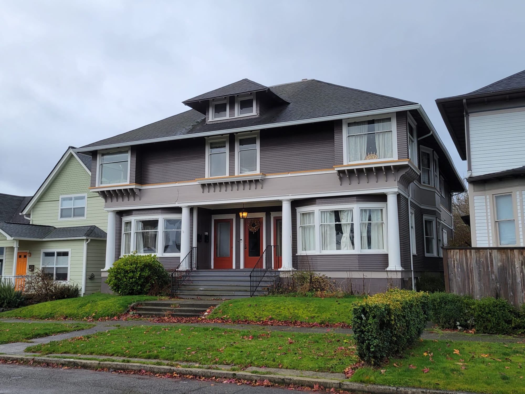 
                     A photo of a grey triplex with red doors that maintains the scale of a large single family house.
                     