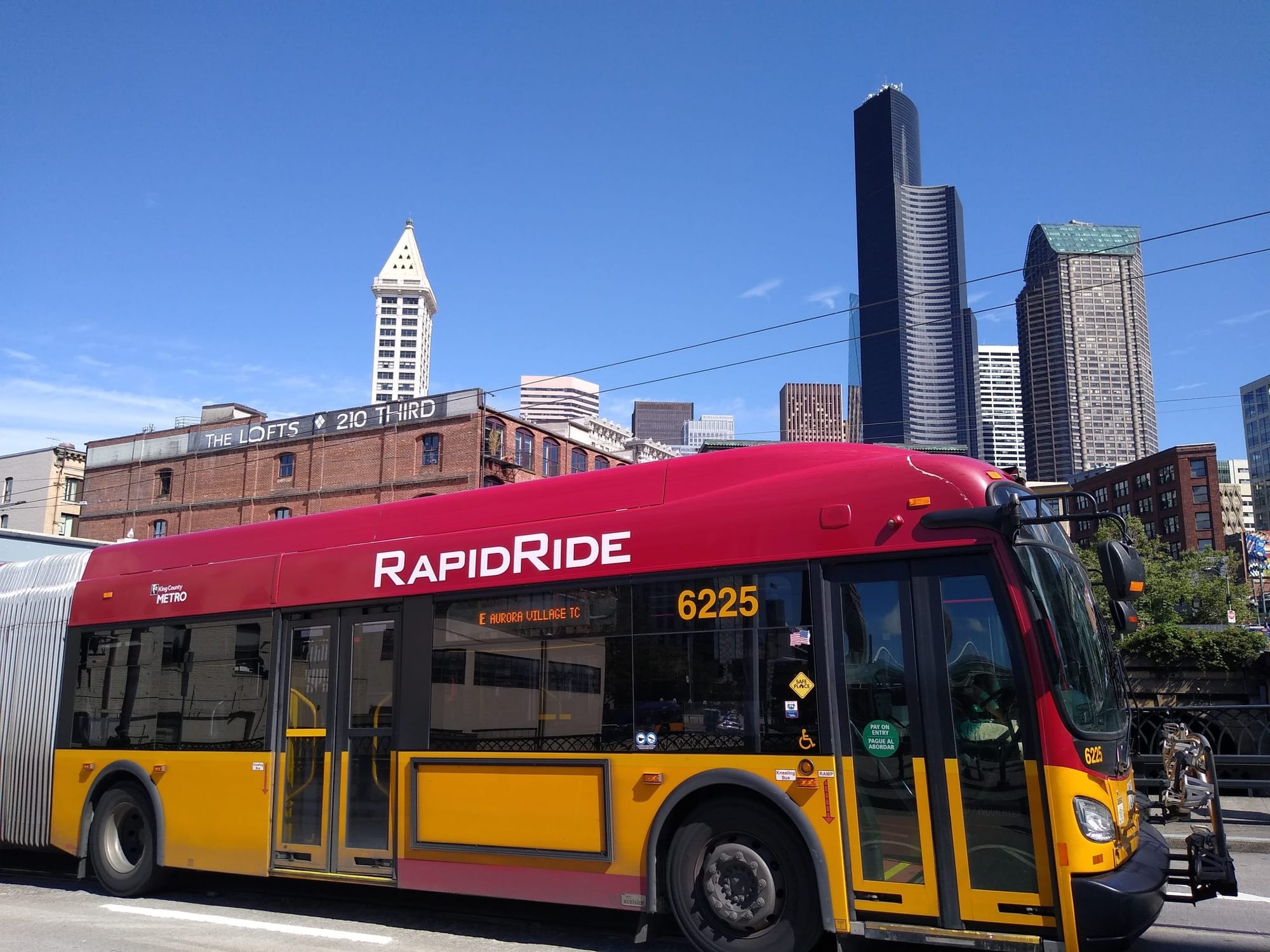 
                     A red and gold RapidRide bus in Pioneer Square with the Seattle skyline in the background.
                     