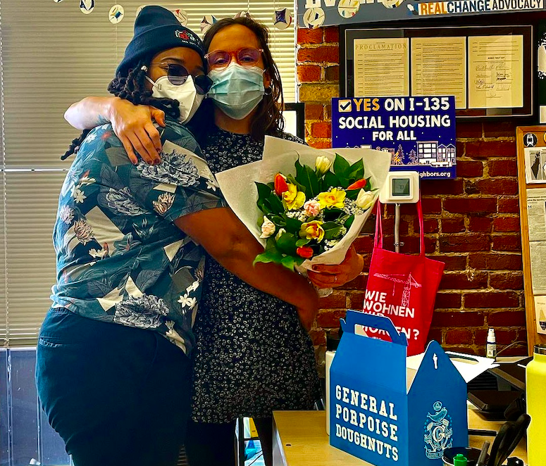 Two people wearing masks hug and hold a bouquet of flowers
