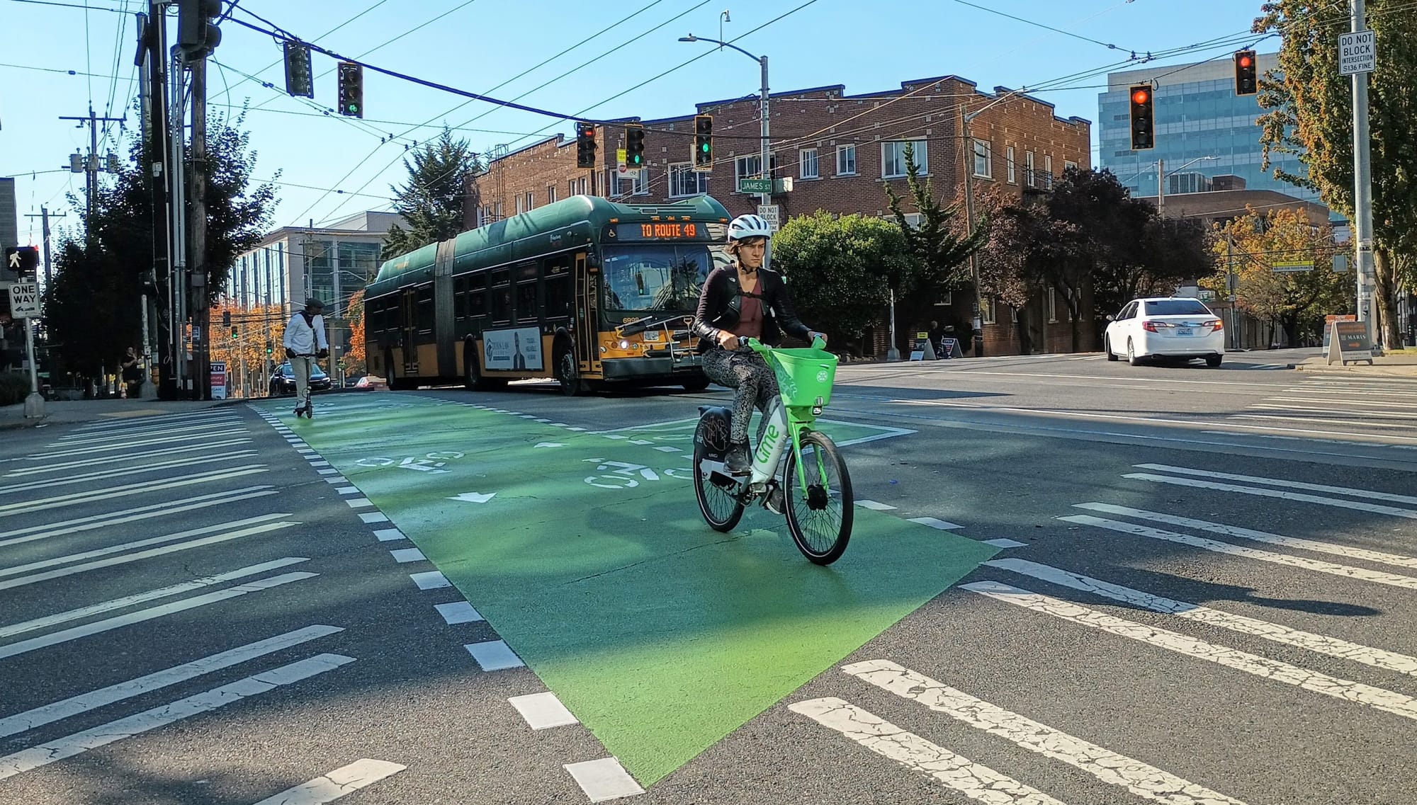 
                     Someone riding a lime bike across a bike lane in Capitol Hill with a bus behind them
                     