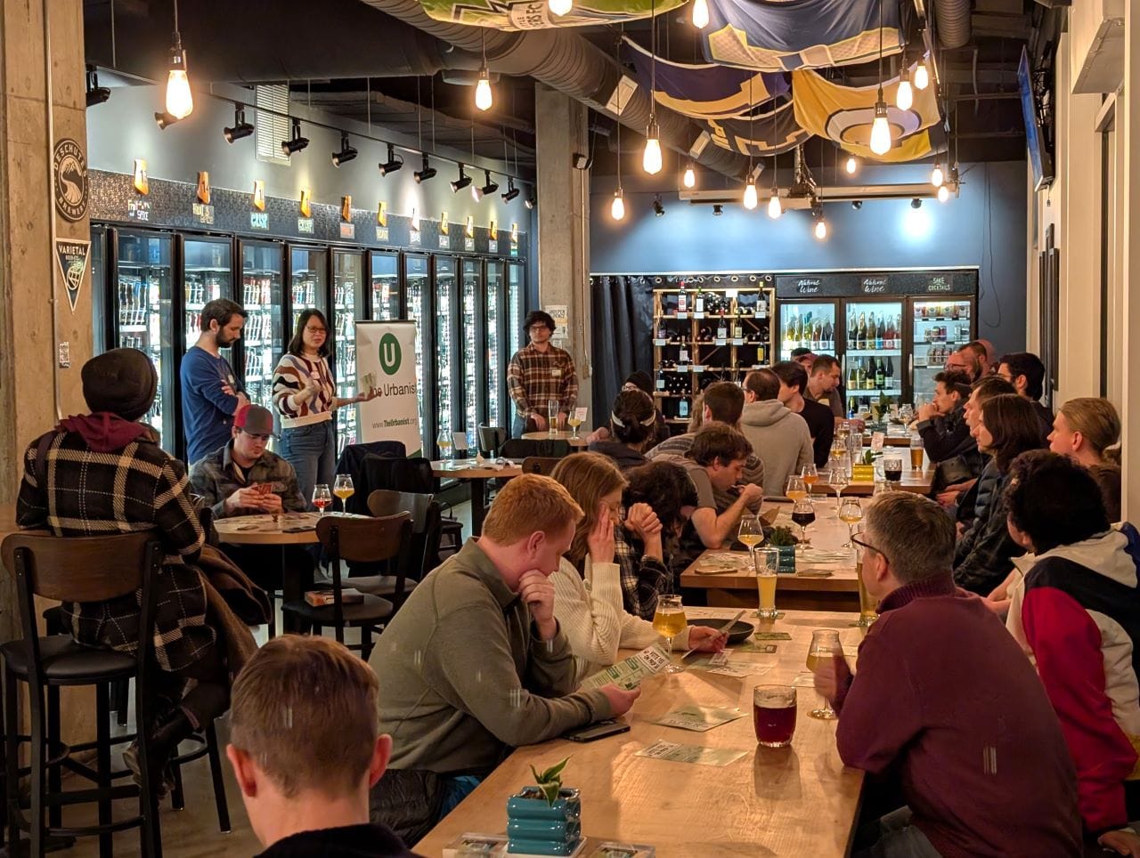 
                     Attendees fill seats in long tables at Teku Tavern two members of House Our Neighbors present to the group.
                     