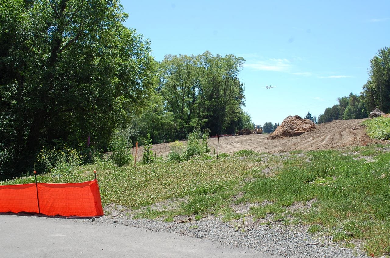 An empty field a pile of wood chips and a skid loader and a plan in the distance