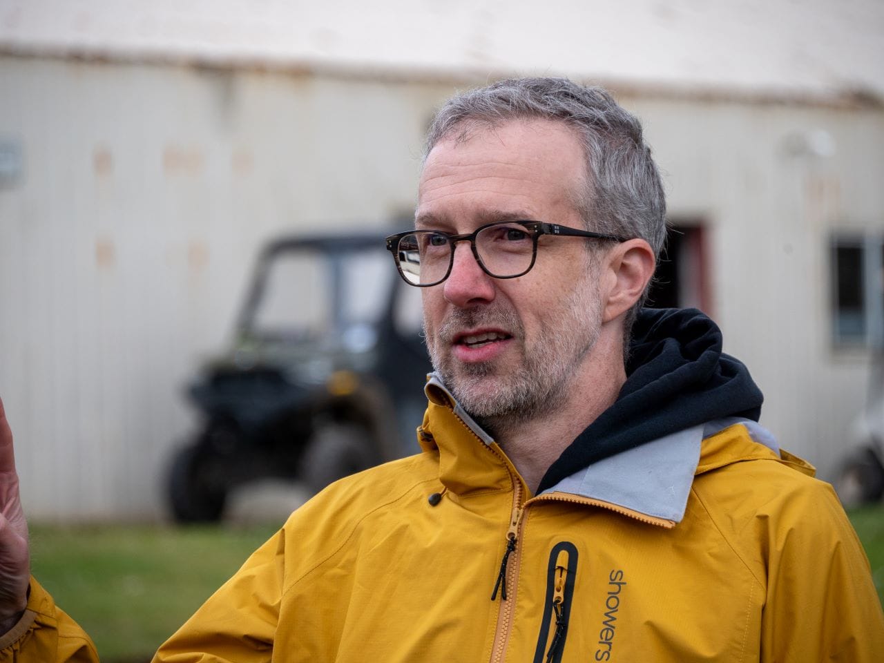 Troy is a man with a short gray beard and glasses wearing a yellow rain jacket.