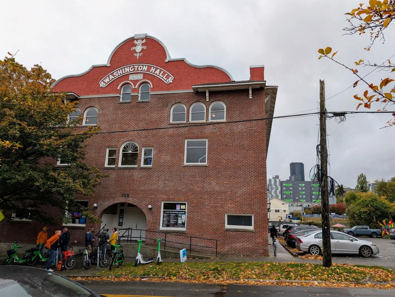 A smattering of bikes and rental scooters are parked out front of the three-story event space. The downtown skyline is visible in the distance.
