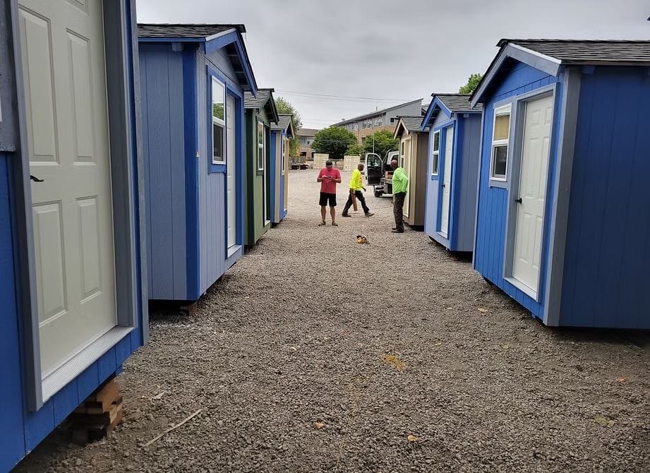 A row of blue tiny homes with three construction workers in the background.