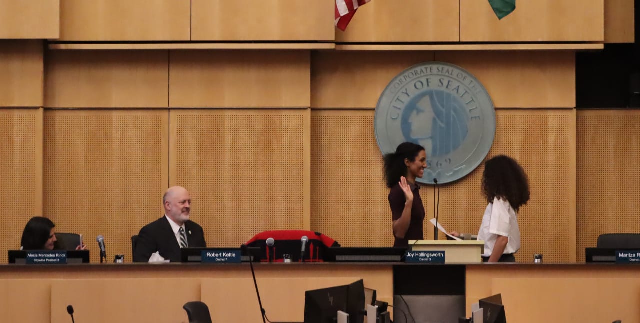 Foster is a black woman standing on the Council dais in front of the City of Seattle seal.