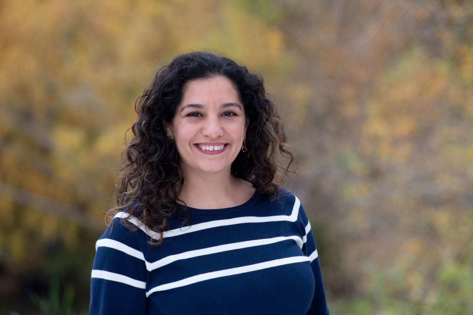 
                     Jenks smiles and has dark wavy hair and wears a striped sweater.
                     