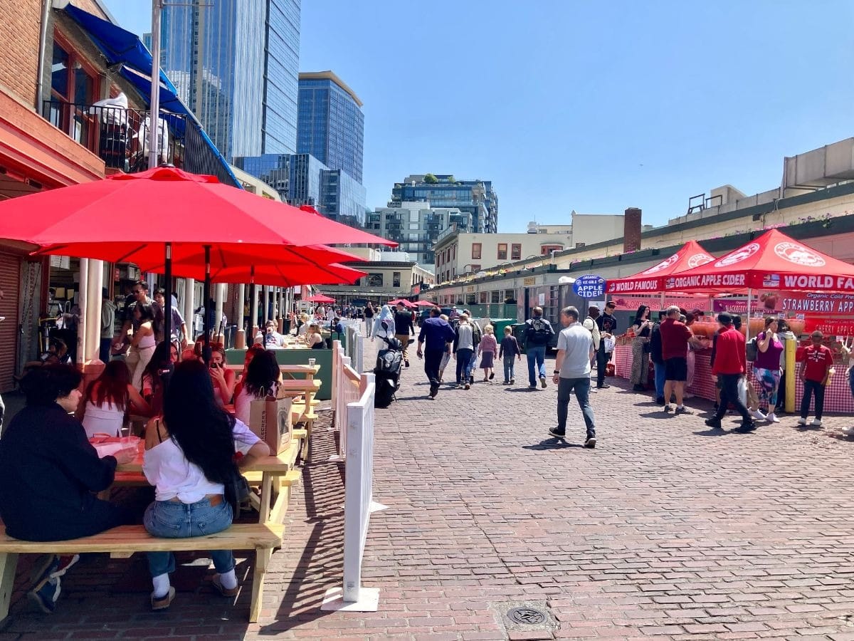Red umbrellas shade sidewalk cafes on the Pike Place cobblestone