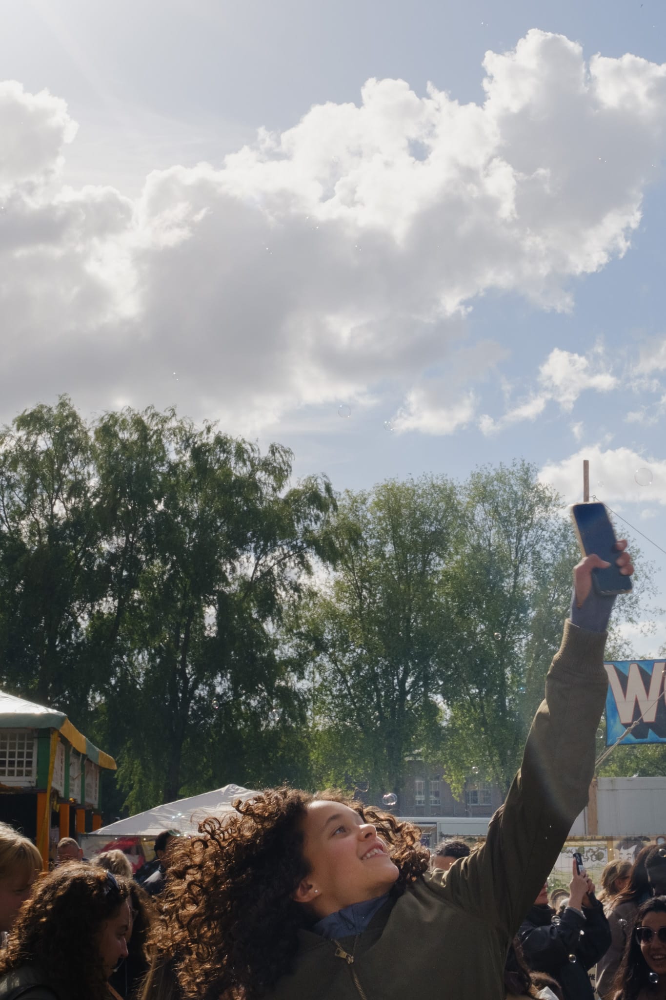 Young woman holding up her phone at an outdoor event in Amsterdam, crowd and trees in the background