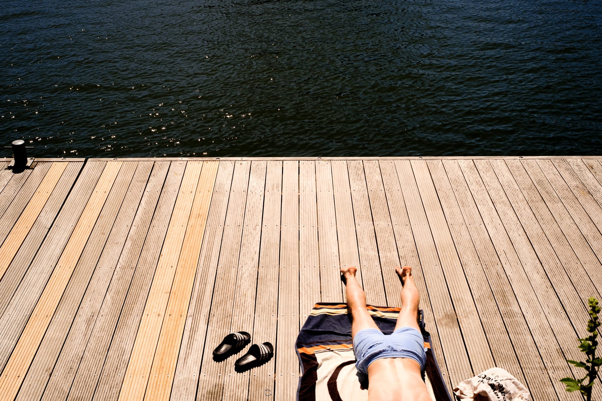 Person relaxing on a wooden dock by the water in Amsterdam, sandals set aside, seen from above