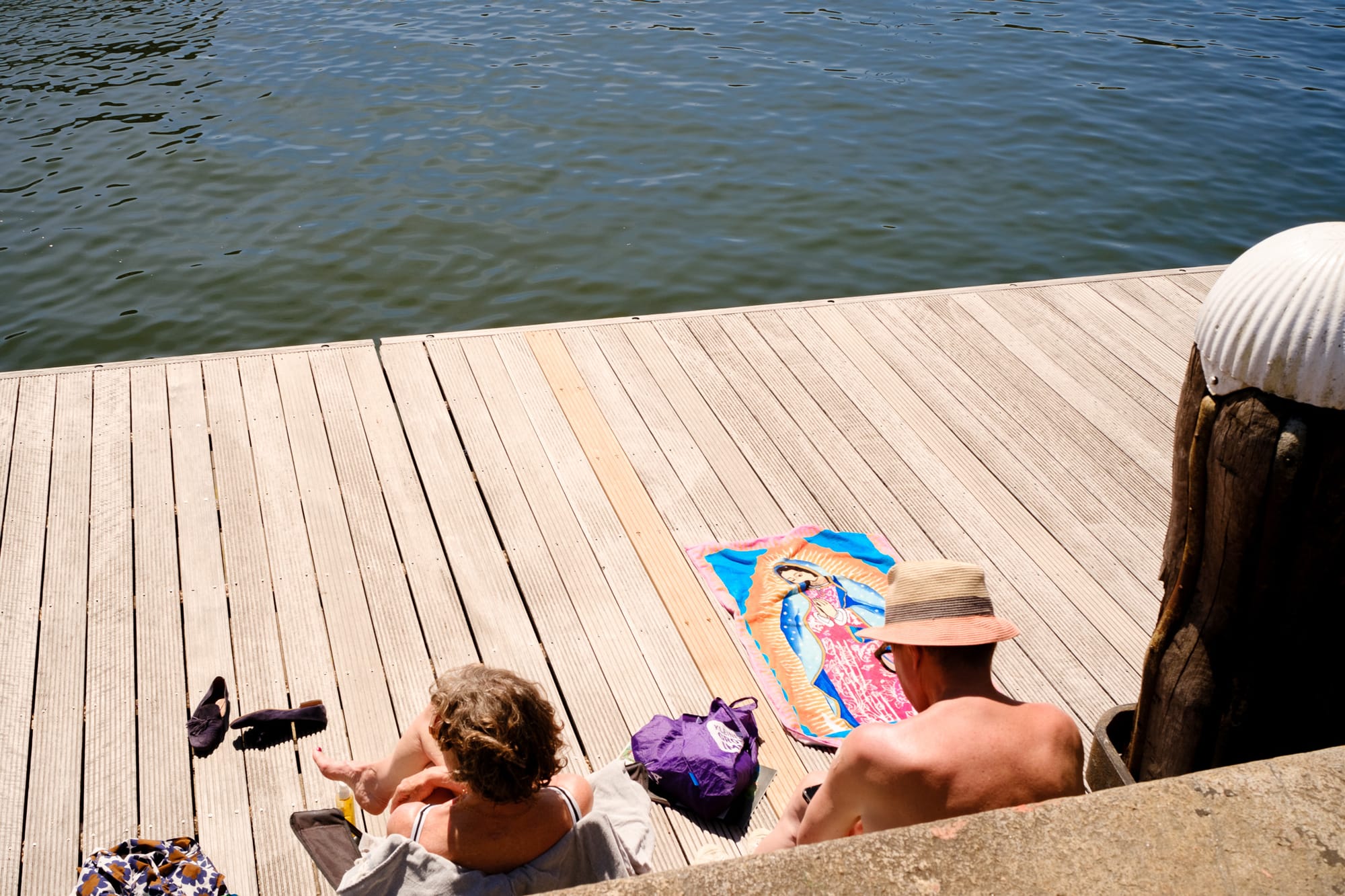 Two people sitting on a wooden dock by the water in Amsterdam, on a sunny day