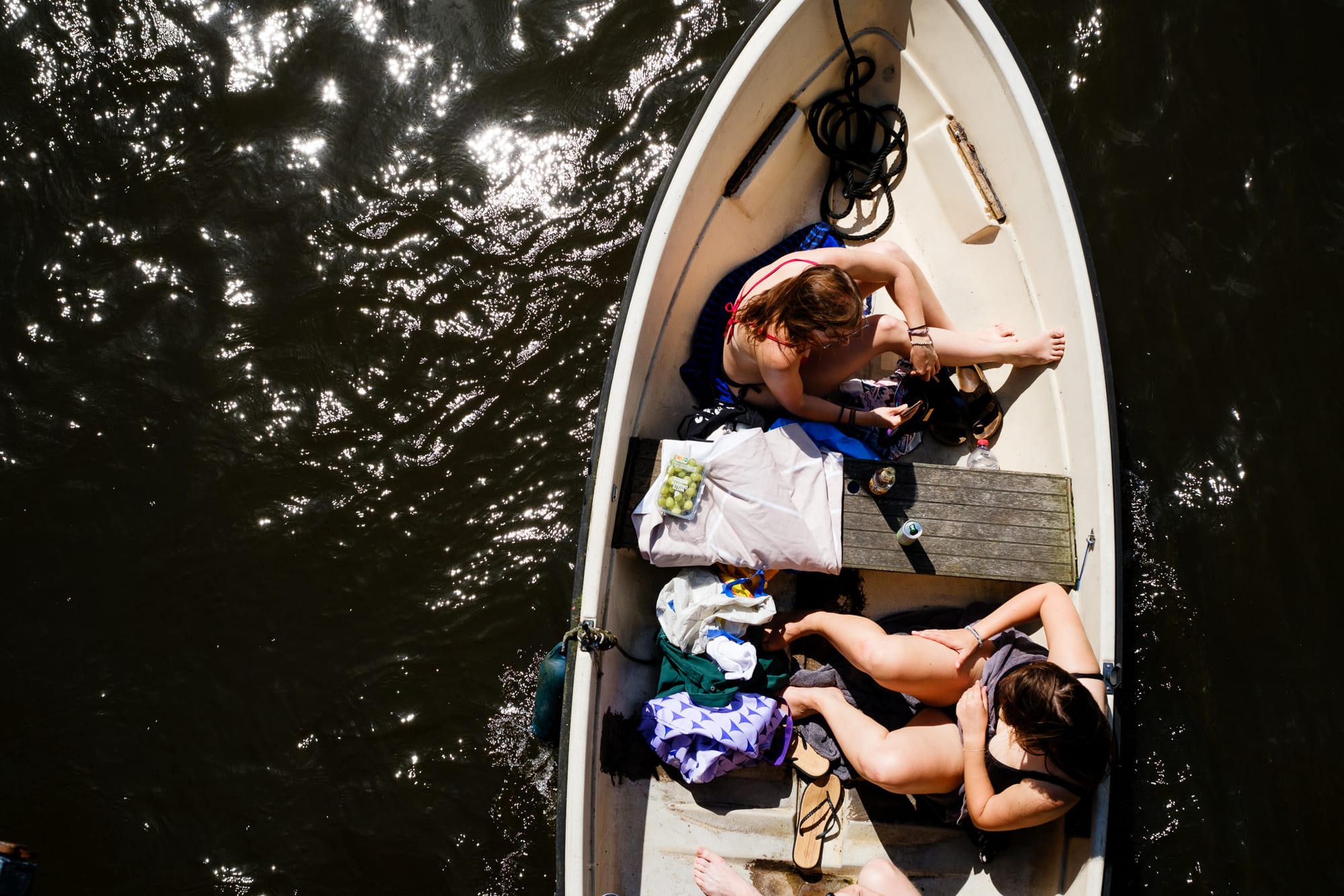 Two people sunbathing in a small boat on an Amsterdam canal, seen from above