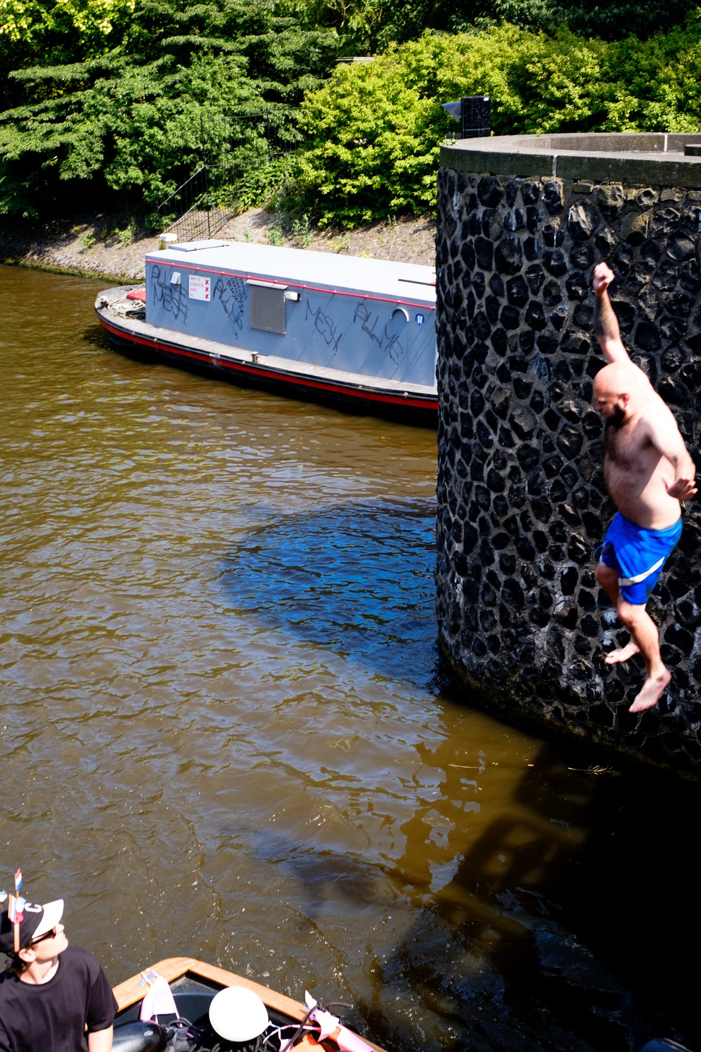 Man jumping off a stone canal wall into the water in Amsterdam