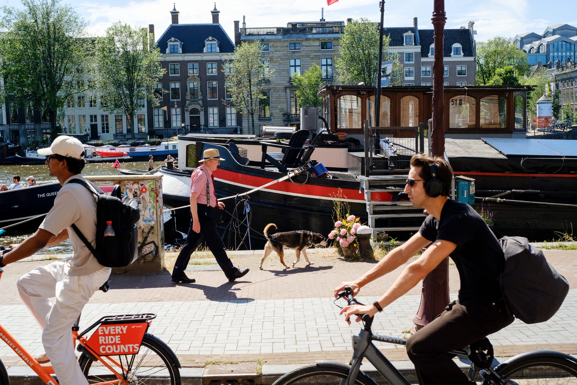 People sunbathing on a wooden dock by the Amstel river, a man in a full suit standing among them