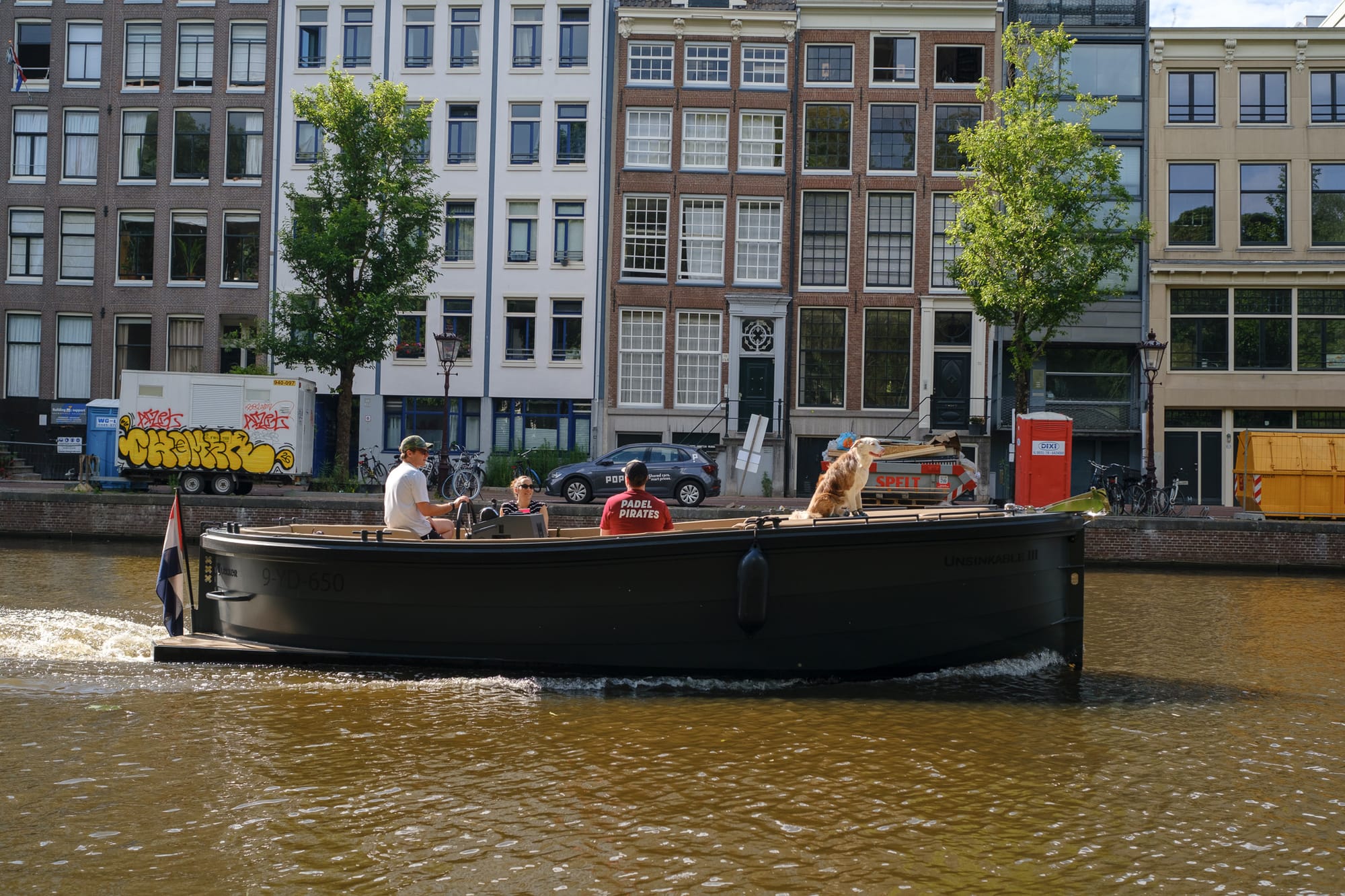 Family on a classic Dutch boat cruising an Amsterdam canal, graffiti wall in the background
