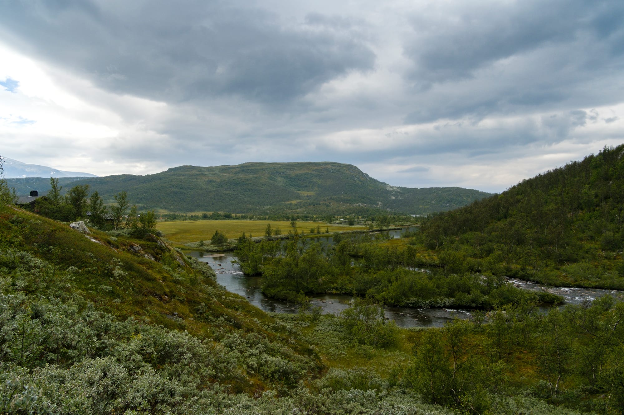 A river running through low green hills on the plateau under heavy cloud.