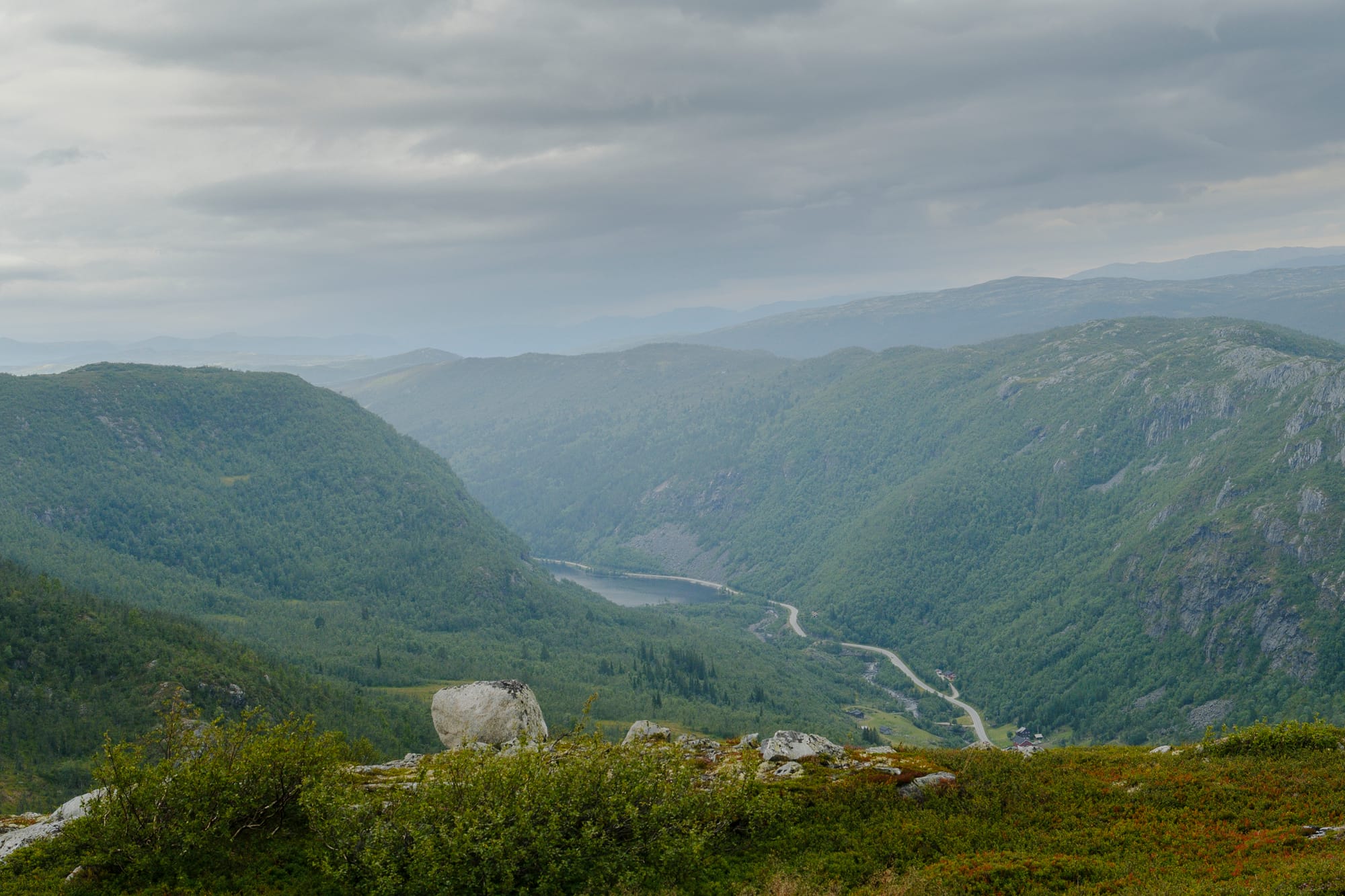 View from the plateau down a deep green valley, with a river winding along the bottom.