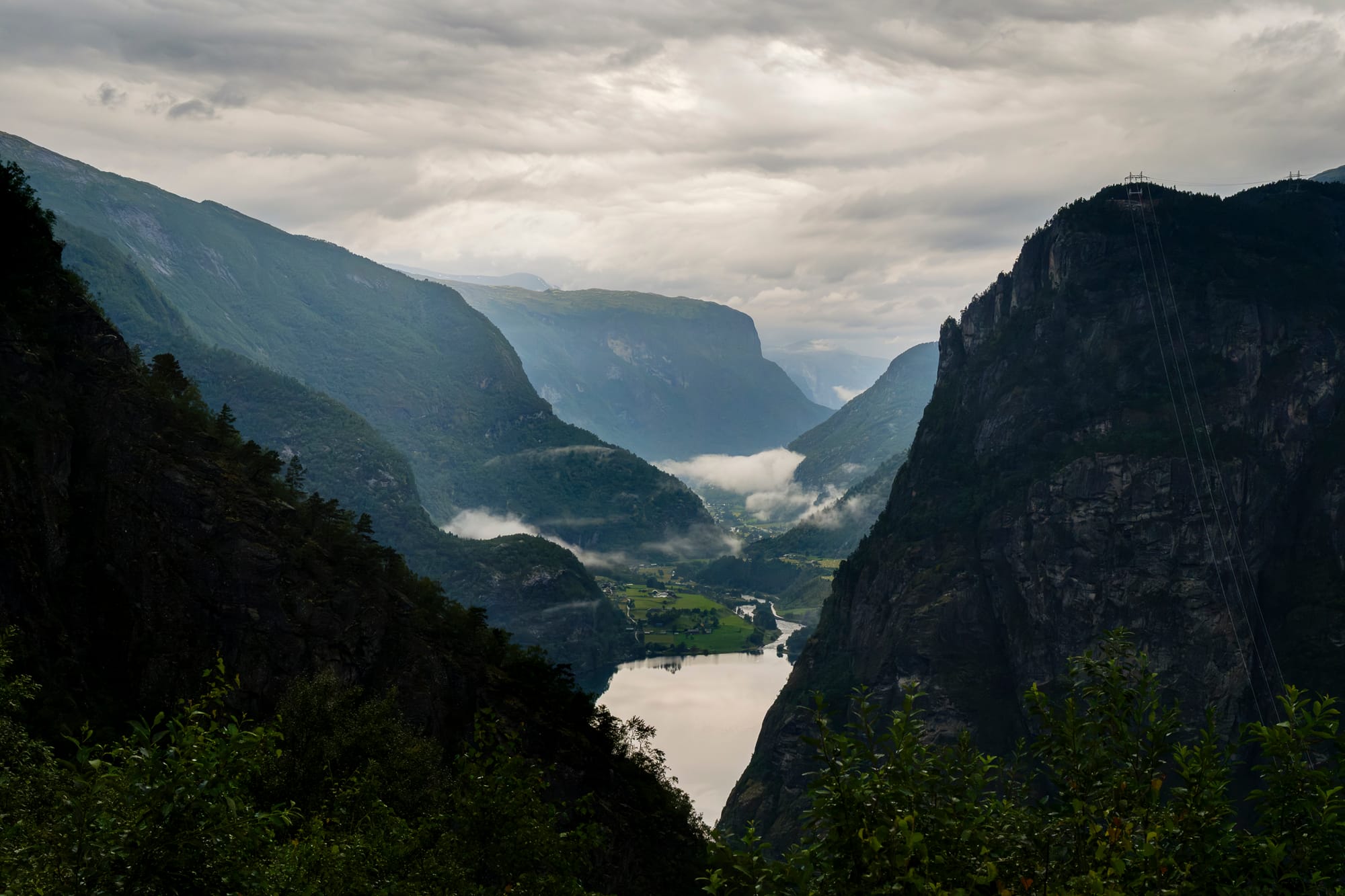A fjord seen from above between steep dark mountainsides, with low cloud in the valley.