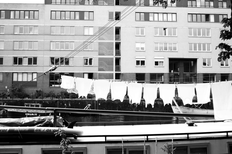 Black and white photograph of laundry hanging on a clothesline on a houseboat in Amsterdam, apartment building in the background