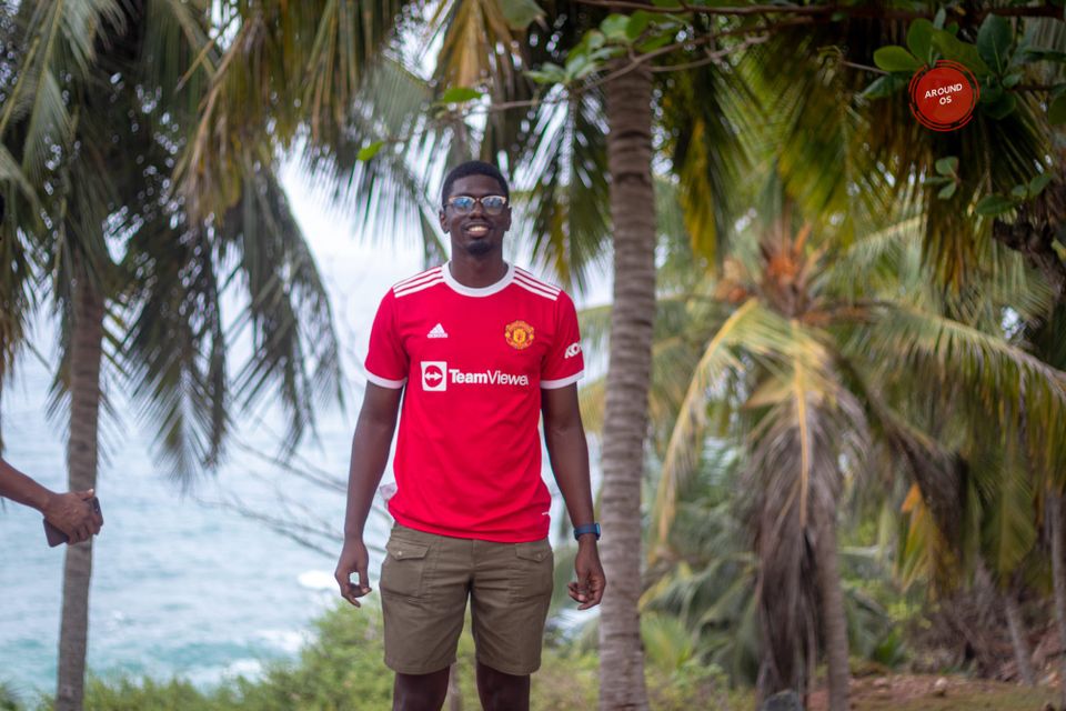Picture of Kwabena standing infron of Palm trees at the southern most part of Ghana, Cape 3 points. Hes wearing a red manchester united Jersey