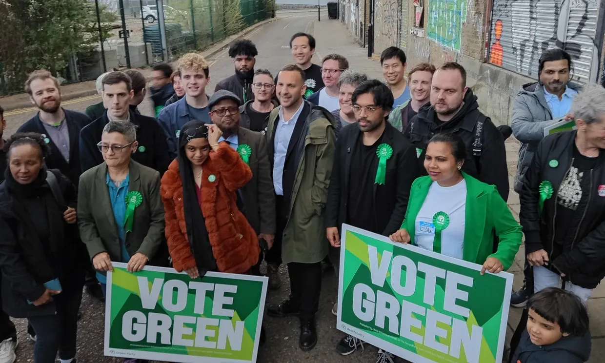Chowdhury stands with Polanski holding VOTE GREEN signs in a group of people. 