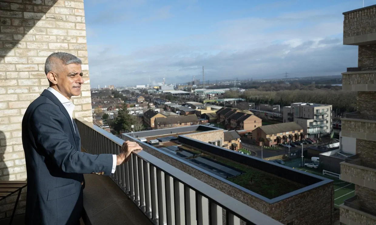 Sadiq Khan looking from a balcony over some housing complexes.