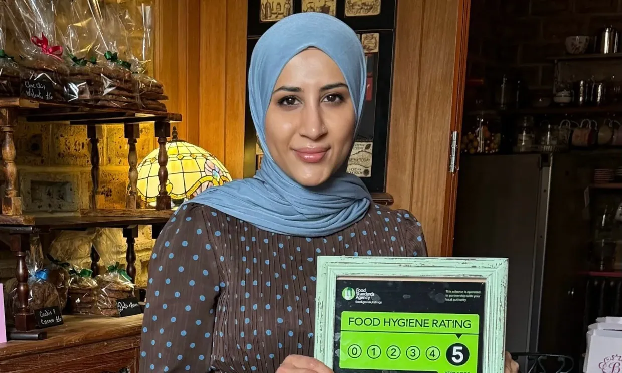 A woman is holding a certificate showing a food hygiene rating of 5 in her kitchen.