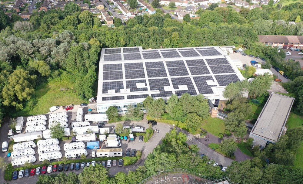 Bottle Yard TBY2 facility, shown from above, a large warehouse with solar panels on its roof surrounded by trees