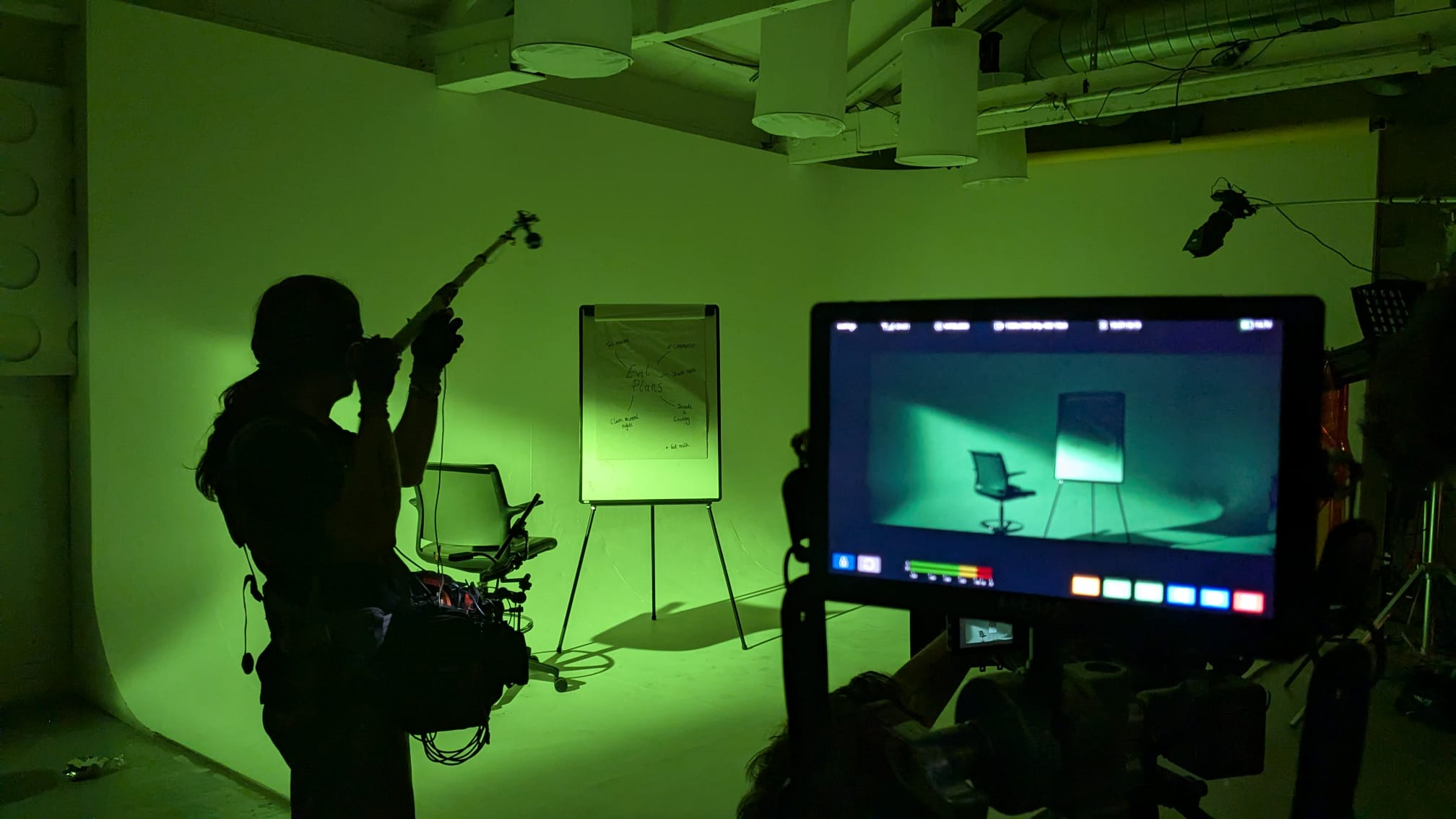 Boom operator on set with a chair, flipchart and monitor.
