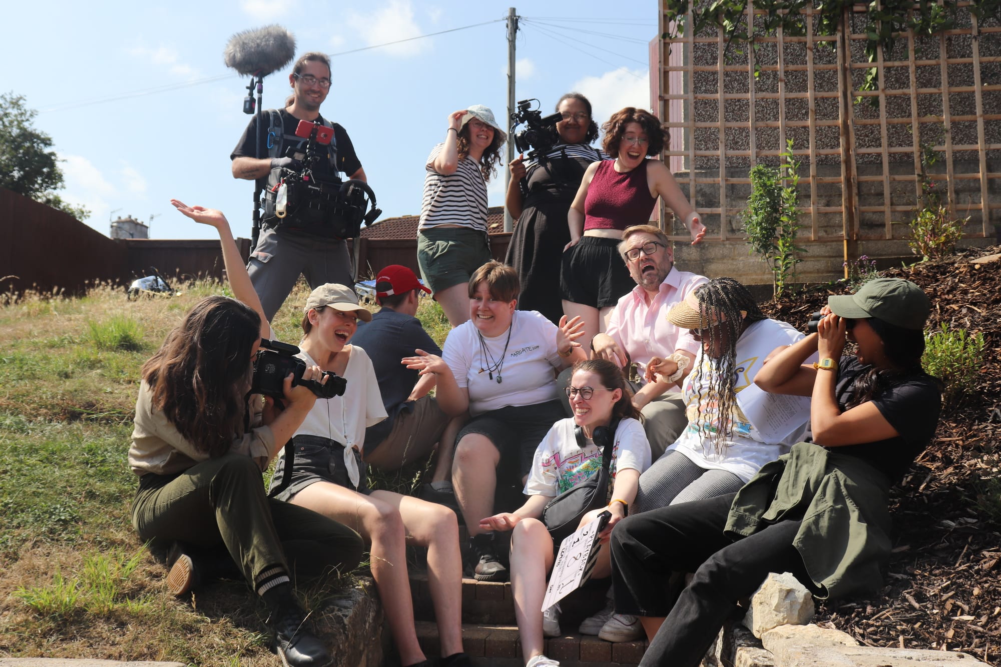 Film crew sitting in a garden pulling funny faces.