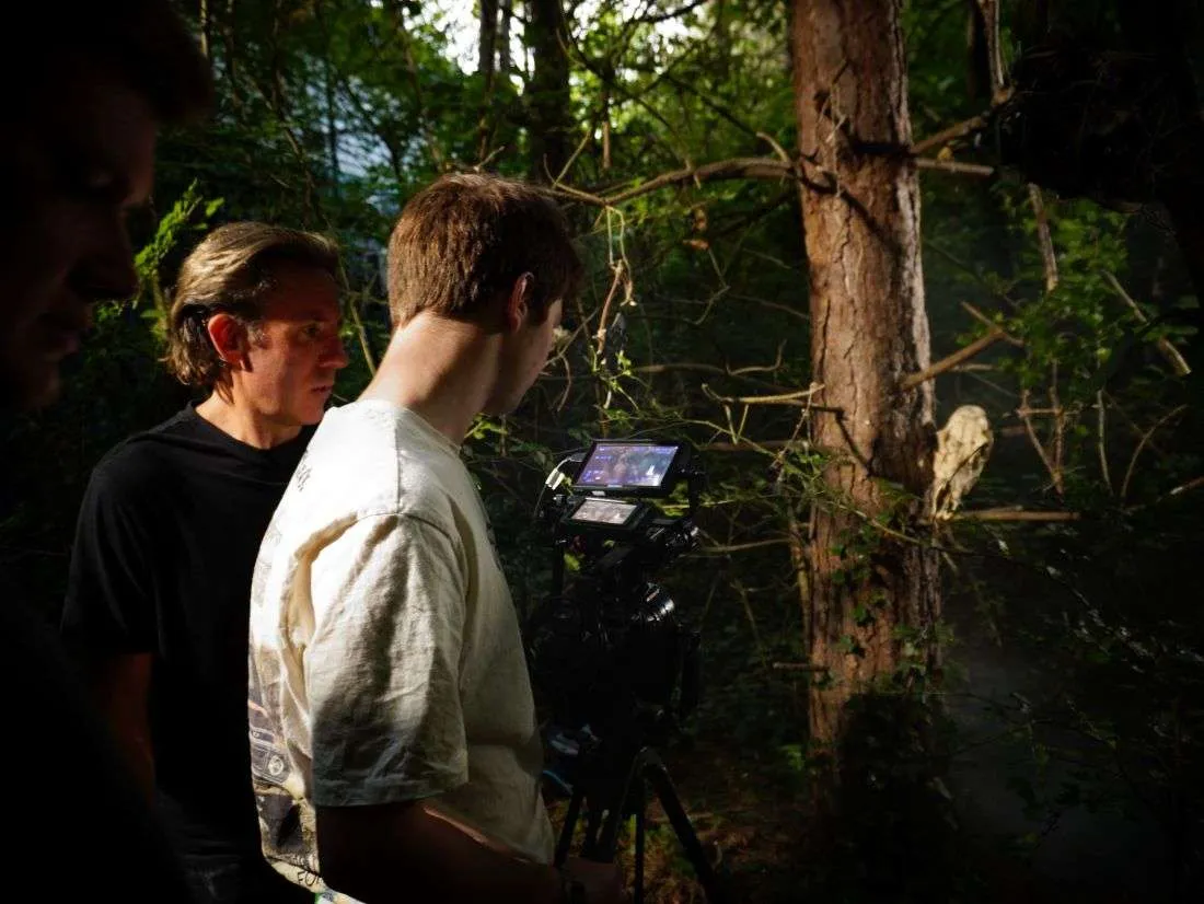 Two filmmakers beside a camera in a forest.
