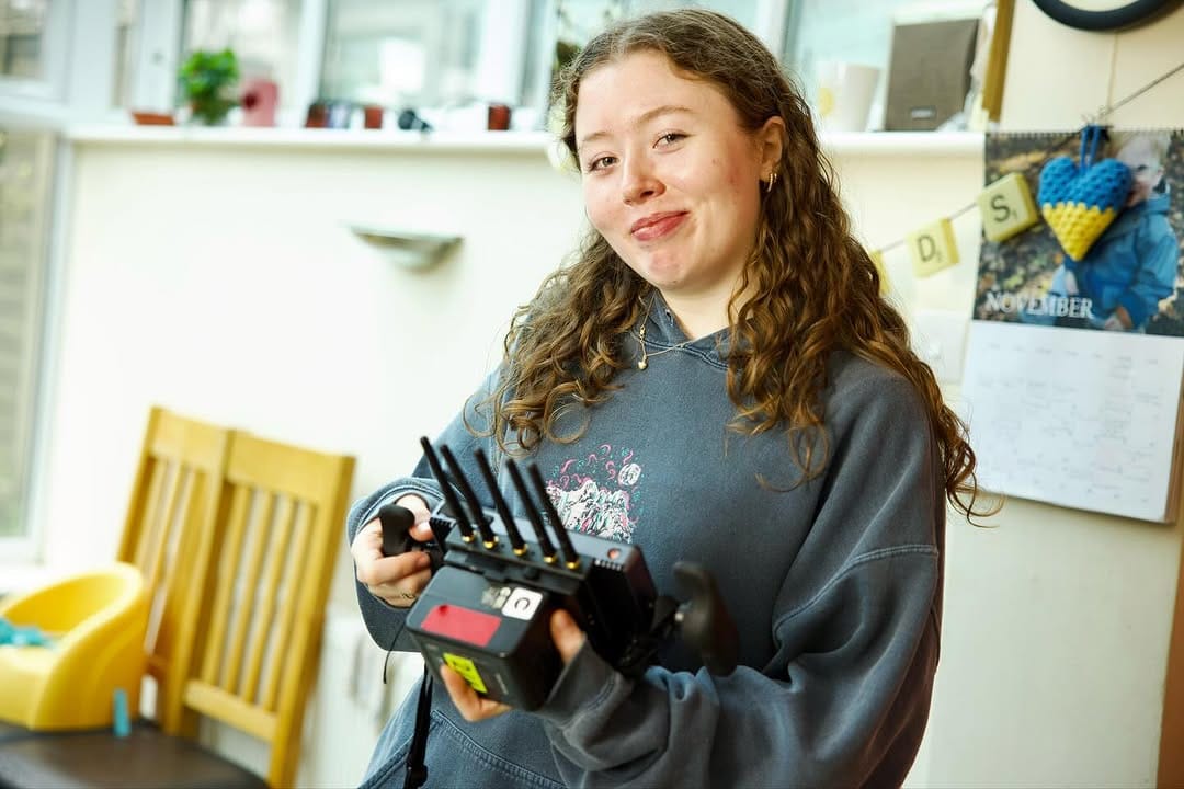 A filmmaker holding a monitor in a living room smiles to camera.
