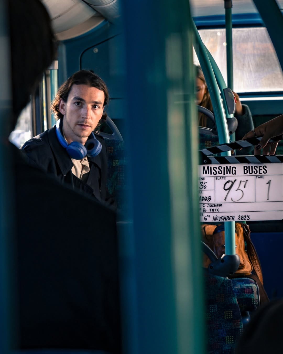 A filmmaker with headphones stands on a full bus film set with clapper board nearby.