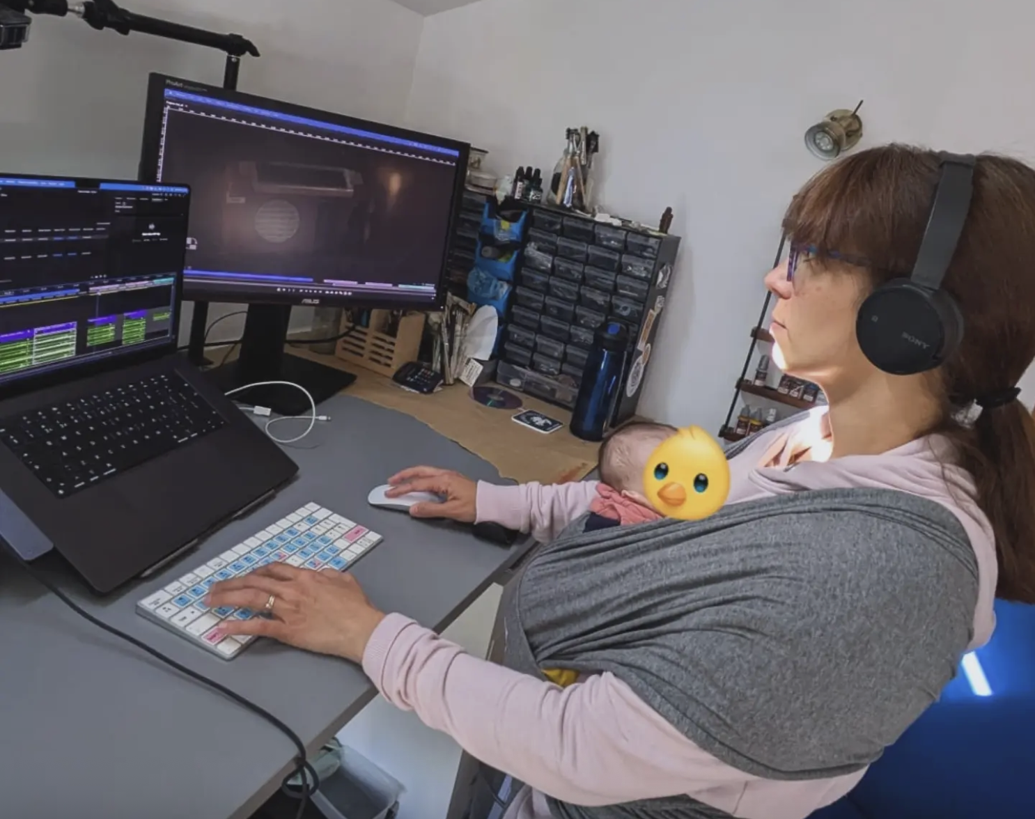 An editor works at a standing desk with a new born baby in a sling.