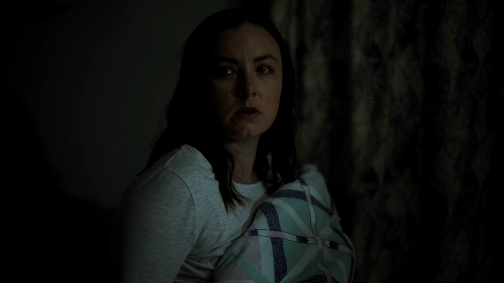 Still from Shadow Peak season 2. Actor/Producer Sarah Dawes looks fearfully in a dark room.