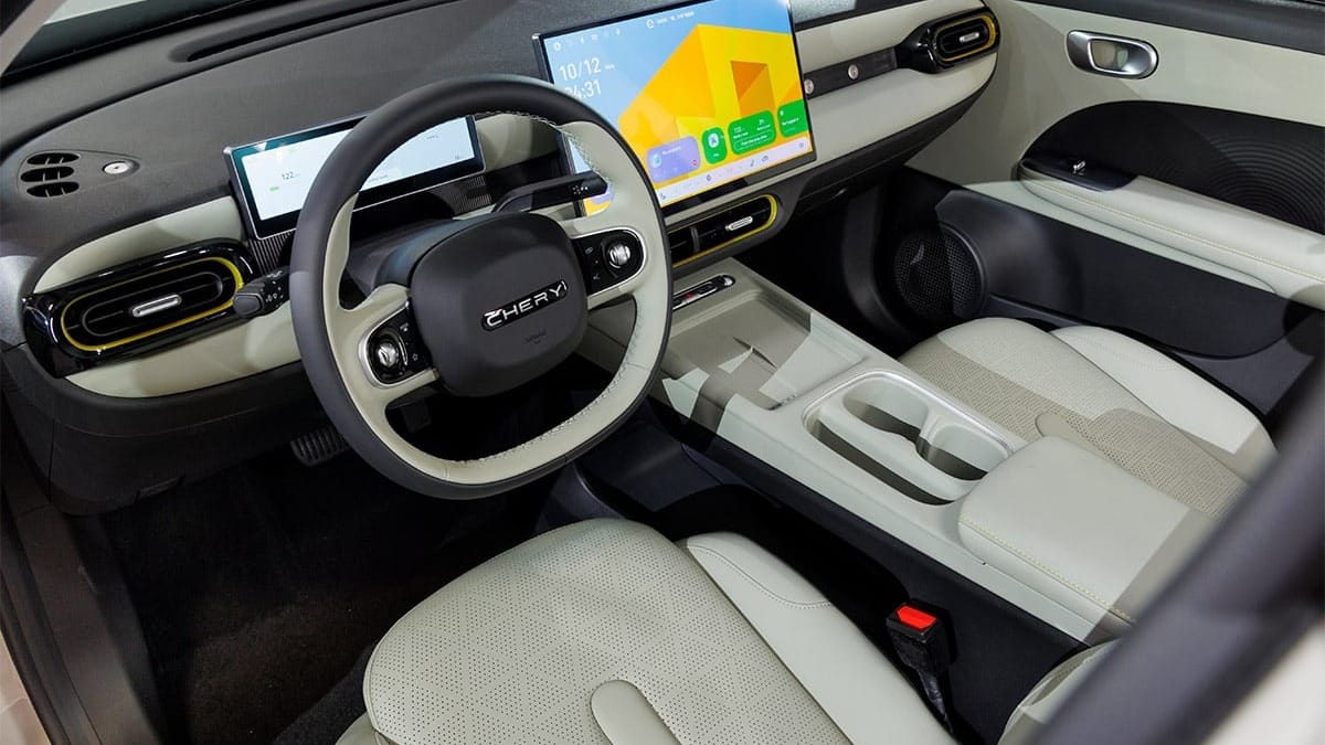 Cockpit des Chery Q mit hellen Sitzen, zwei Bildschirmen und gelben Akzenten an den Lüftungsdüsen.