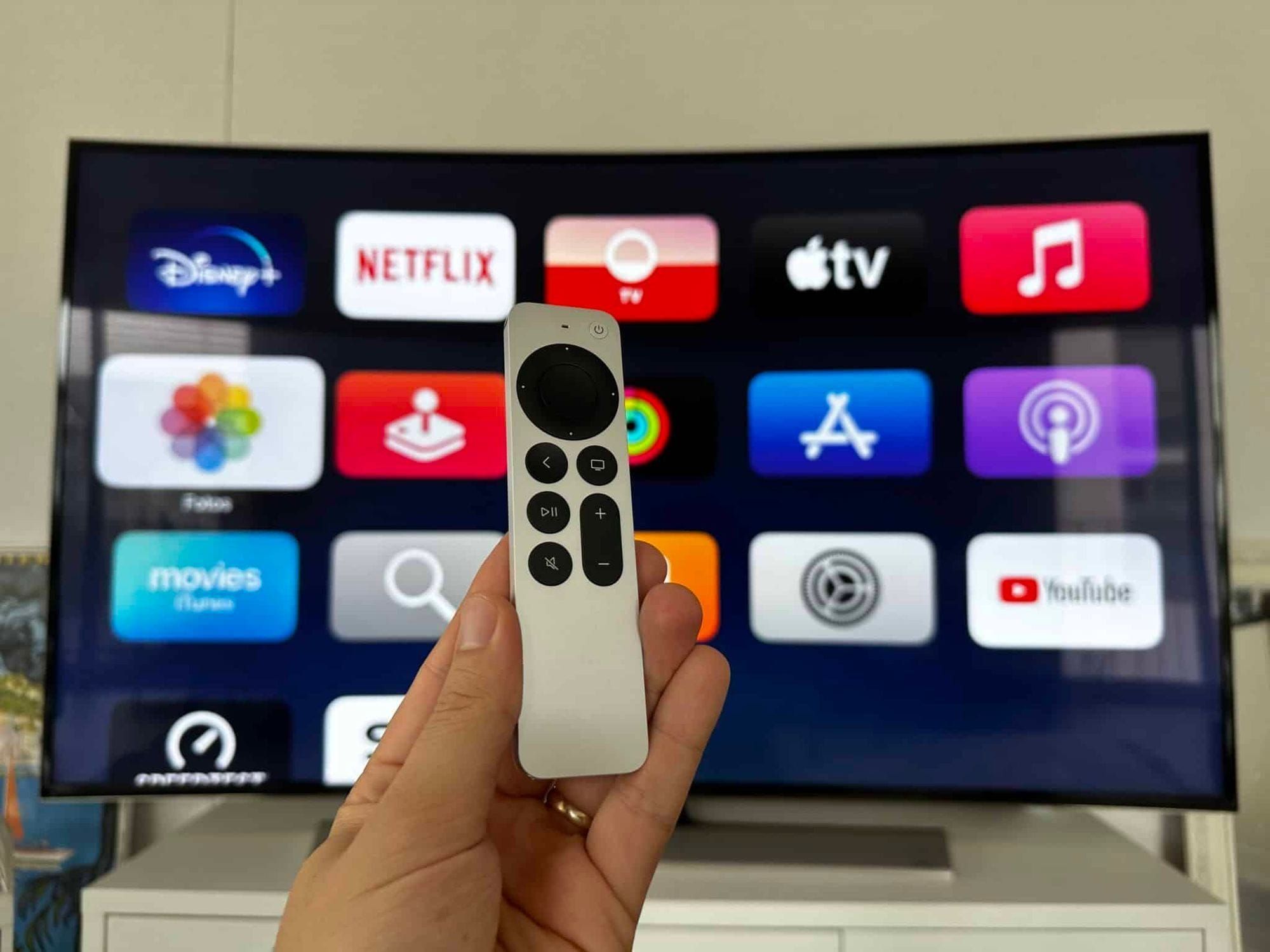 Apple TV 4K, App-Übersicht im Hintergrund und Fernbedienung im Vordergrund