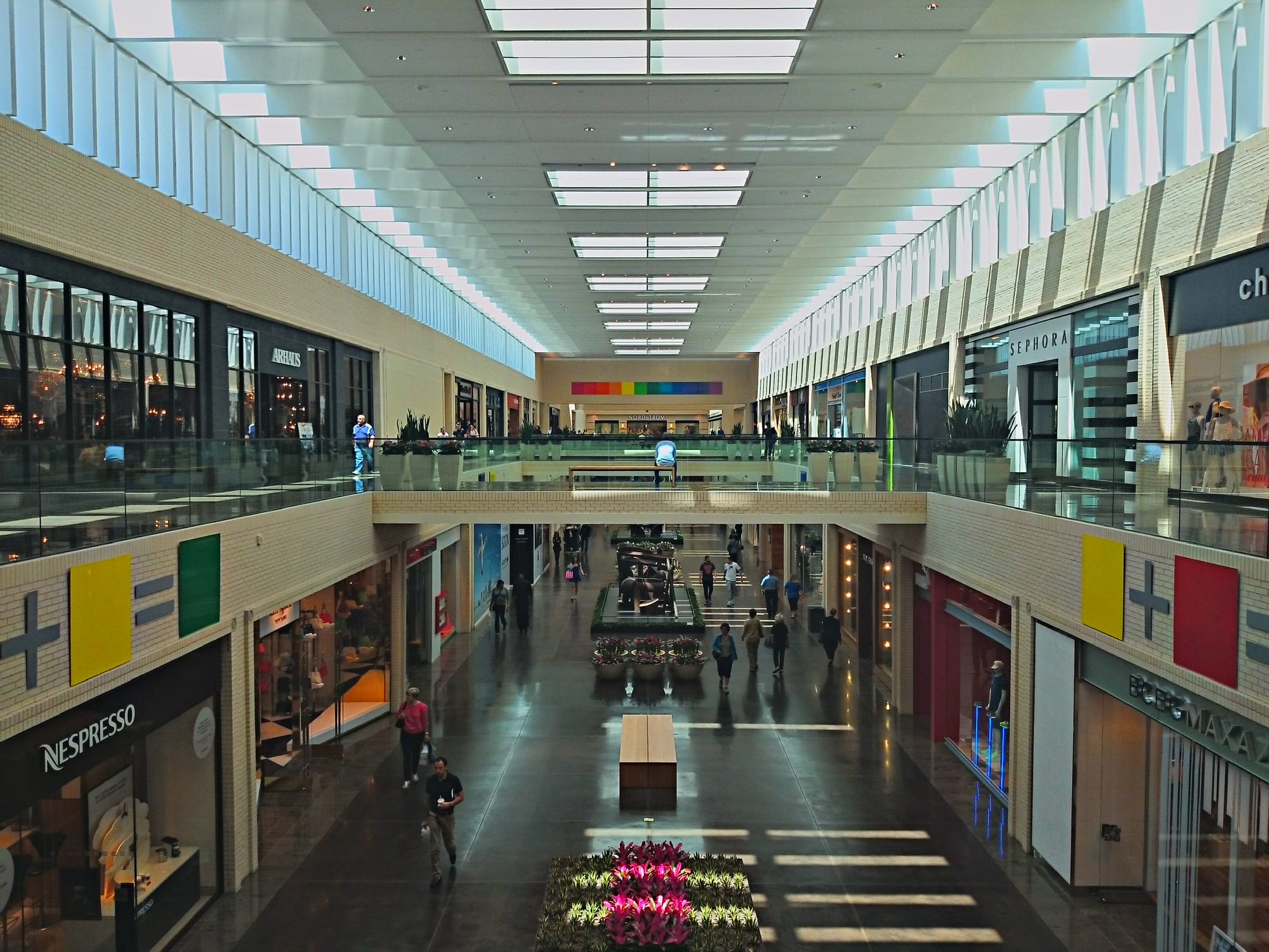 Two-level concourse at NorthPark Center in Dallas, with colored Color Equations panels mounted along both walls and a rainbow spectrum band above the Nordstrom entrance.