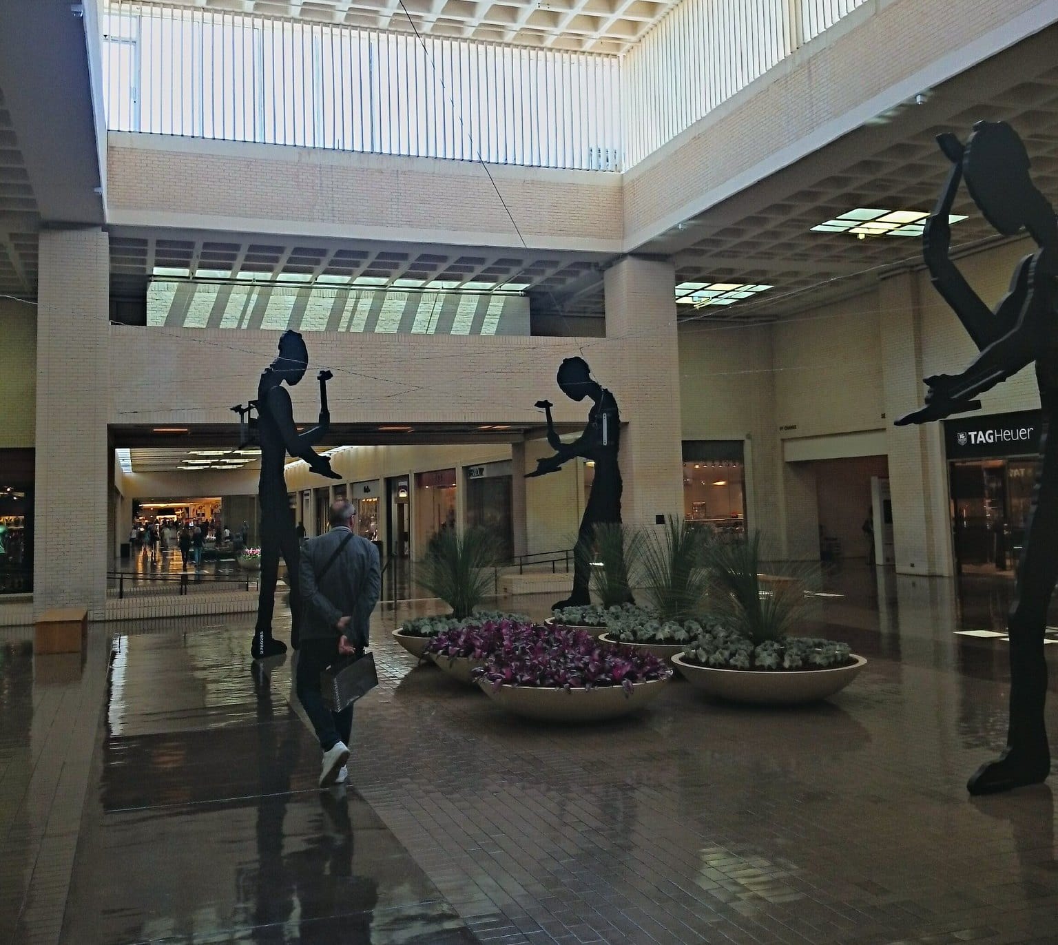 Three of Jonathan Borofsky's Five Hammering Men, tall black silhouetted figures with motorized hammering arms, in SouthCourt at NorthPark Center in Dallas.