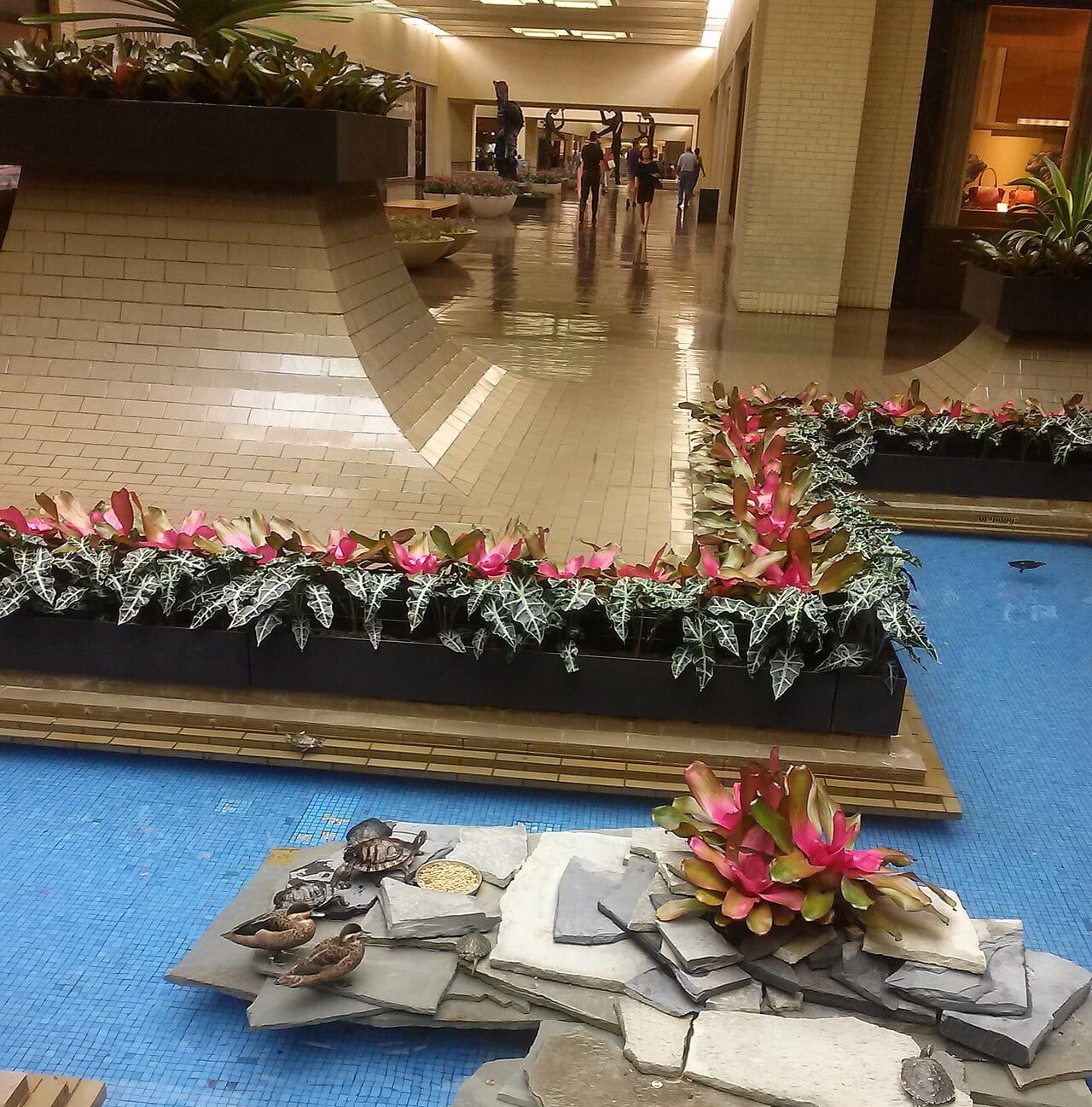 NorthPark Center's indoor pond with live turtles and ducks on a slate island, and the silhouettes of Jonathan Borofsky's Five Hammering Men visible down the concourse behind it.