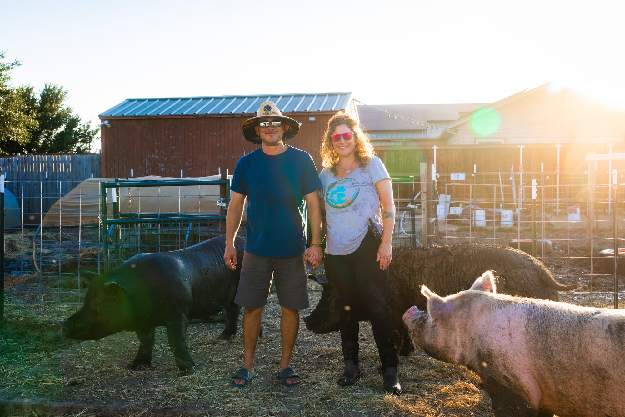 Alli and Justin, founders of The Zend, stand with three of their rescued pigs