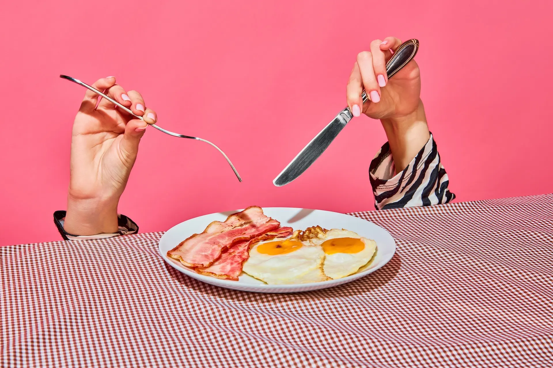 Hands holding a knife and fork about to eat a fry-up