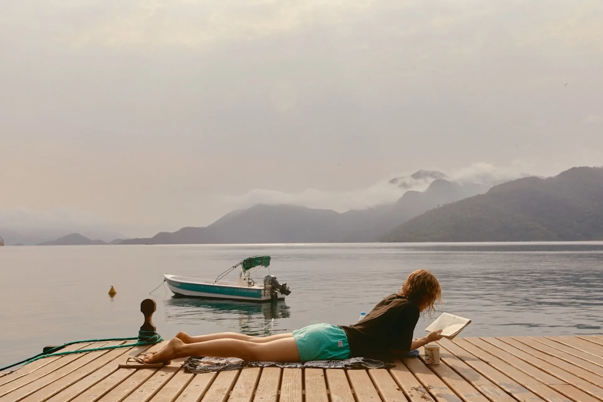 Woman reading by the water with mountains in the background